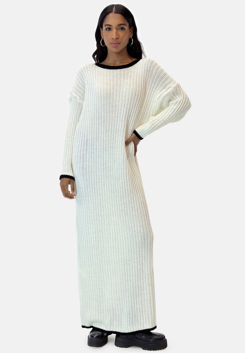 Langes weißes geripptes Strickkleid mit schwarzem Besatz am Ausschnitt und an den Ärmeln, das einen lockeren Schnitt und lange Ärmel hat.