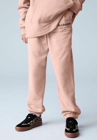 Heledad roosa dressipüksid, millel on elastsed mansetid, lõdvestunud lõige ning vasakul reiel asuv "ALLSAINTS" logo. Sobitatud leopardimustriliste tossudega.