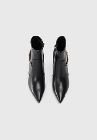Bottines en cuir noir avec un bout pointu, fermeture éclair sur le côté et détails matériels décoratifs. Texture lisse avec une finition brillante.