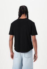 Black, short-sleeve t-shirt with a round neckline and a curved hem. Fabric appears soft and smooth. Back view shows braiding in hair.