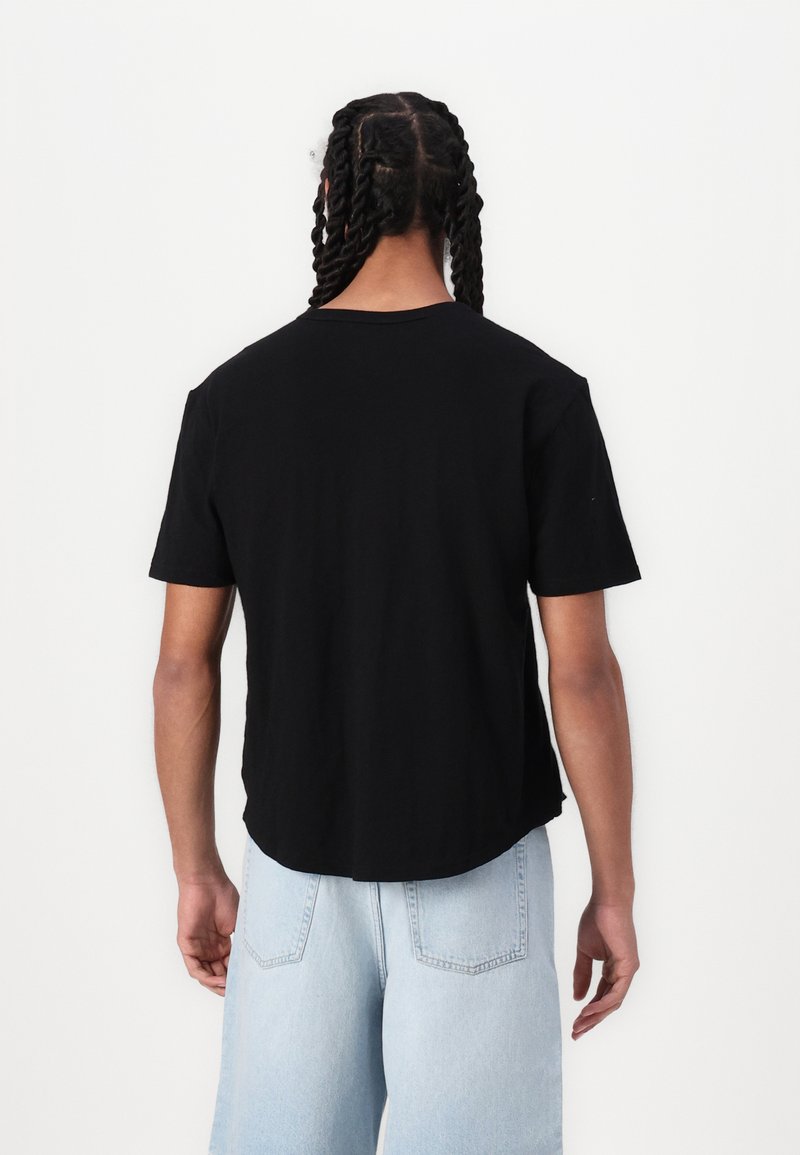 Schwarzes T-Shirt mit kurzen Ärmeln, rundem Halsausschnitt und abgerundetem Saum. Der Stoff wirkt weich und glatt. Die Rückansicht zeigt einen geflochtenen Zopf.