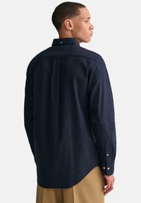 Marineblauwe button-up shirt van textuurstof, met een achterste schouderpas en manchetten met één knoop, gecombineerd met beige broeken.