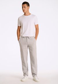 Pantalon rayé gris clair avec une taille à cordon de serrage, associé à un t-shirt blanc à manches courtes et des baskets blanches.