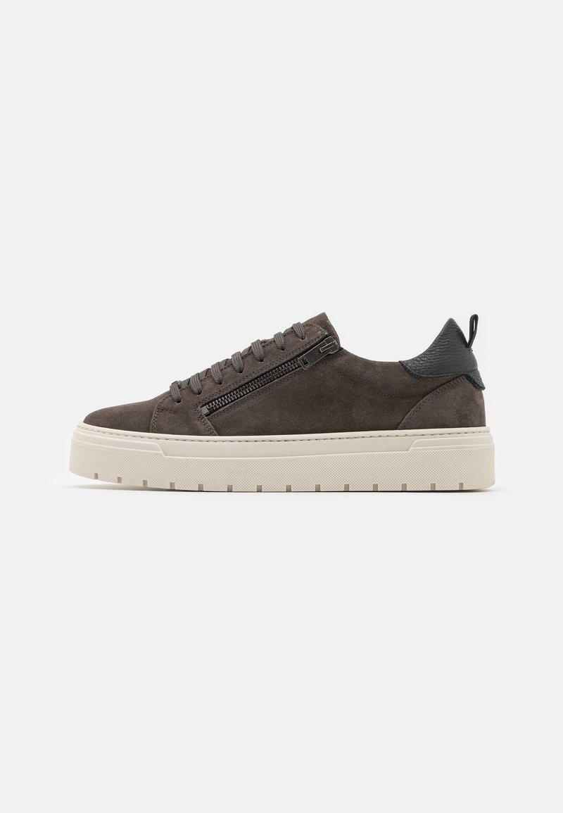 Baskets basses en daim marron foncé avec lacets à l'avant, fermeture éclair latérale, languette de talon noire et semelle épaisse blanc cassé sur fond blanc.