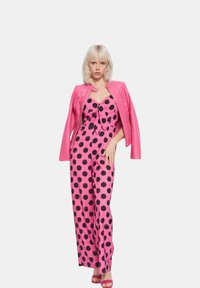 Mono rosa con estampado de lunares, con detalle de lazo y perneras anchas, combinado con una chaqueta de cuero rosa. El conjunto se complementa con tacones rosas.