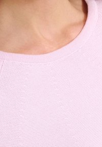 Närbild av en ljusrosa stickad tröjkrage som bärs av en person, som visar texturerad tyg och hud i nackområdet.