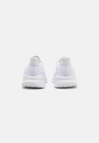 Baskets de sport blanches avec une tige lisse et texturée, des semelles rembourrées et un logo discret au niveau du talon. Design minimaliste et forme symétrique.