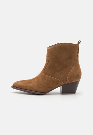 Brauner Wildleder-Stiefelette mit spitzer Zehe, gestapeltem Blockabsatz und Zuglasche hinten, im Profil vor einfarbigem Hintergrund gezeigt.