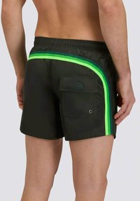 Costumi da bagno neri con doppie strisce verdi sui lati, una tasca posteriore con patta e un tessuto leggero e testurizzato.