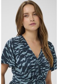 Tmavě modré šaty se světle modrým abstraktním vzorem, s výstřihem do V a řasením vpředu, krátkými rukávy a hladkou látkou.