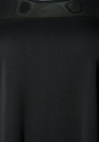 Tessuto nero con texture e piccole perforazioni nella zona superiore della schiena, che mostrano due zone di ventilazione ai lati.