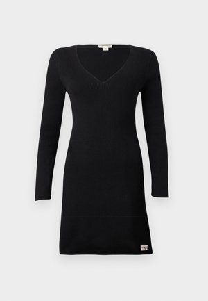 Schwarzes geripptes Strickkleid mit langen Ärmeln, V-Ausschnitt und einem kleinen Markenpatch nahe dem Saum auf einem schlichten hellen Hintergrund.