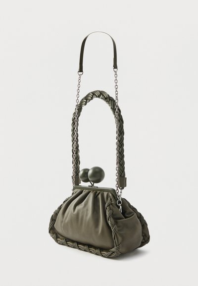 Τσάντα ώμου σε ελιά πράσινο, κατασκευασμένη από απαλό ύφασμα, με πλεκτή λαβή, μεταλλικές αλυσίδες και δύο στρογγυλά κούμπωμα στο πάνω μέρος.