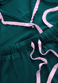 Turkos pyjamaset med rosa volangkrage, hjärtformad detalj och en elastisk midjeresår med matchande rosa band. Tyg som är mjukt och slätt.