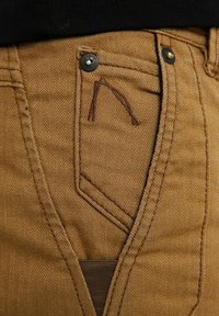 Bruna herringbone-byxor har en framficka med sömdetaljer, metallbeslag och en texturerad tygkvalitet med en lätt lyster.