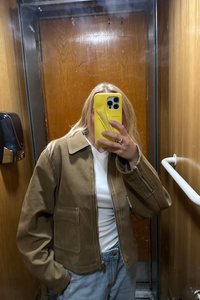 Giacca marrone a trama con colletto, tasche frontali e dettagli di cucitura visibili. Indossata sopra una maglietta bianca e jeans azzurri chiari.