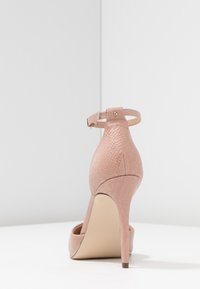 Zapato de tacón alto en rosa claro con un patrón texturizado de piel de serpiente, correa al tobillo y un diseño de punta afilada sobre un delgado tacón de aguja.