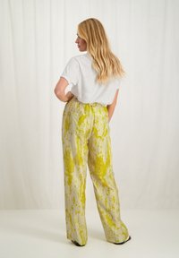Linnen blendbroek met een losse pasvorm, met een geel abstract patroon op een lichte achtergrond. Gecombineerd met een grijze top met korte mouwen.
