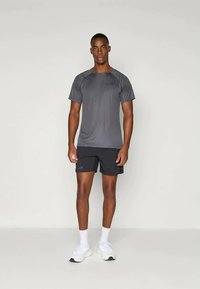 Grå atletisk T-shirt med korte ærmer og et subtilt logo, parret med sorte shorts, båret med hvide sneakers og ankel-lange sokker.