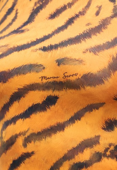 Ύφασμα σε σχέδιο τίγρης σε πορτοκαλί και μαύρο, με απαλό υλικό. Δείχνει το χαρακτηριστικό "Marine Serre" σε διακριτική θέση κοντά στο μοτίβο.