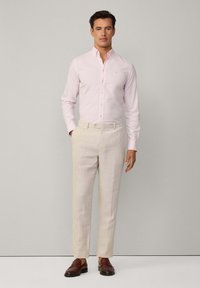 Light pink button-down shirt paired with beige linen trousers. Brown leather shoes complete the outfit. Simple design and tailored fit are evident.