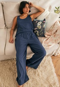 Set di top in cotone blu navy e pantaloni a gamba larga in un morbido tessuto, con una vita elastica. Cuscino a motivi floreali audaci nelle vicinanze.