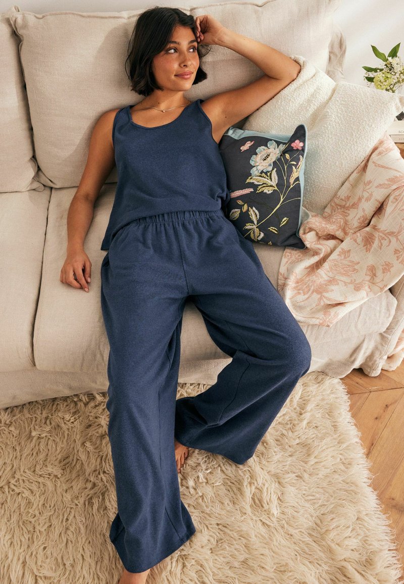 Set di top in cotone blu navy e pantaloni a gamba larga in un morbido tessuto, con una vita elastica. Cuscino a motivi floreali audaci nelle vicinanze.