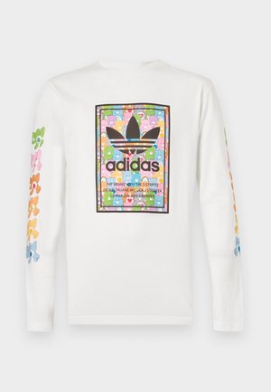Hvid skjorte med lange ærmer med farverigt bamsemønster på ærmerne og Adidas-logo med bamser i en rektangel på brystet.