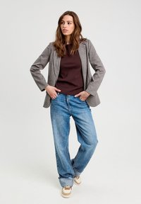 Blazer à carreaux gris sur un haut marron, associé à un jean bleu ample et des baskets beiges. Le blazer a une coupe ajustée et un design structuré.