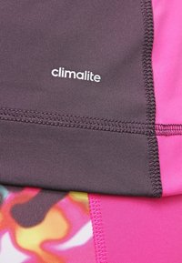 Odzież sportowa Climalite z ciemnofioletową górną częścią, jaskraworóżową dolną częścią oraz żywym, wielokolorowym wzorem na tkaninie.