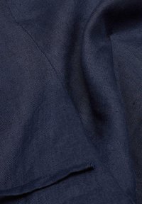 Marineblauwe stof met een gladde textuur, voorzien van een subtiel geweven patroon. De stof lijkt licht gekreukt en valt elegant.