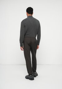 Dunkelgrauer Strickpullover mit hohem Kragen, kombiniert mit leichten braunen Hosen und schwarzen Sportschuhen. Glatte Textur und lässige Passform.