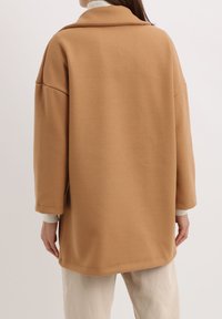 Abrigo de mezcla de lana color camel con un ajuste relajado, cuello de chal y hombros caídos. Presenta mangas largas y una textura suave.