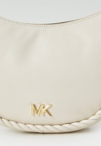 Kreminė dirbtinės odos rankinė su kreiviu siluetu, aukso užtrauktuku ir n braided tekstūroje apačioje, puošta metaliniu "MK" logotipu.