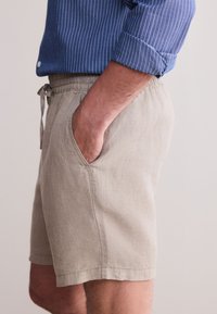 Pantaloncini beige in lino con vita elastica e coulisse, dotati di tasche laterali e orlo sopra il ginocchio.