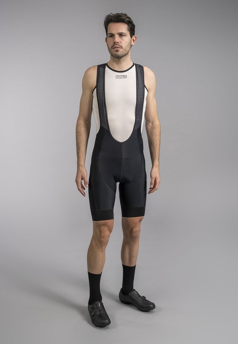 Black cycling bib shorts with a textured mesh upper. Features padded seat, fitted leg cuffs, and contrasting lighter top panel.