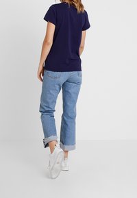 Mörkblå bomulls t-shirt med korta ärmar, ihop med ljusblå uppvikta jeans. Vita sneakers med texturerade sulor avslutar looken.