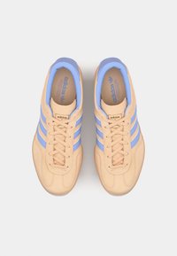 Par de sapatilhas Adidas bege com riscas azuis e forro interior, vistas de cima em fundo branco.