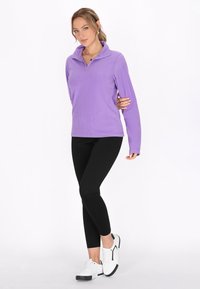 Lilla fleece pullover med halv-zip krave, parret med sorte leggings og hvide sneakers med sorte accenter. Glat tekstur og tætsiddende design.