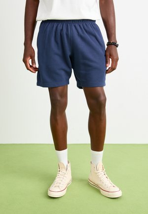 Navy blue cotton shorts with an elastic waistband, side pockets, and a classic fit, paired with high-top beige sneakers and white socks.