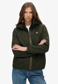 Ciemnozielona wodoodporna kurtka z kapturem, zamkiem błyskawicznym z przodu i elastycznymi mankietami; z naszywką z logo na piersi i pomarańczowymi akcentami.