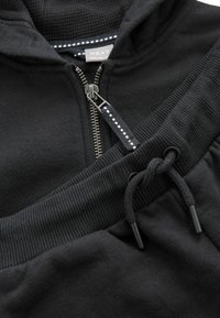 Schwarzer Zip-Hoodie mit gerippten Bündchen und Kordelzug an der Taille. Verfügt über einen silbernen Reißverschluss und kontrastierende Textur am Kragen.
