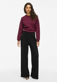 Sweatshirt bordeaux avec un col rond et des manches longues associé à un pantalon noir à large jambes texturé avec une taille élastique.