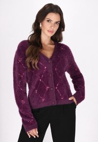 Cardigan morado y esponjoso con escote en V, patrón de lentejuelas en forma de diamante y cinco botones redondos, combinado con pantalones negros.