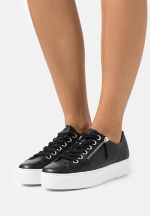 Schwarze Leder Sneakers mit abgerundetem Zehenbereich, weißer Plateau-Sohle, schwarzen Schnürsenkeln und seitlichem Reißverschluß-Detail. Strukturierte Oberfläche und metallische Akzente.
