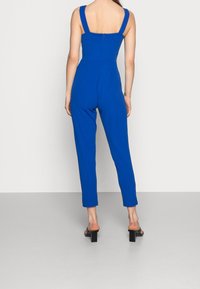 Mono azul con tirantes anchos, cuerpo ajustado y piernas estrechas. Confeccionado con una tela suave, con cremallera trasera. Diseño casual adecuado para diversas ocasiones.