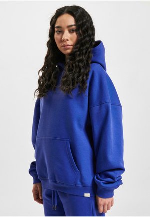 Blue pullover hoodie in soft fabric with a large front pocket, oversized fit, and drawstring hood. Includes ribbed cuffs and hem.