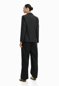 Blazer nero a righe sottili abbinato a pantaloni neri larghi. L'outfit presenta una texture liscia e una silhouette aderente con un design strutturato.