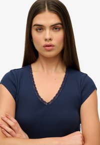 Marineblauwe geribde t-shirt met korte mouwen en een V-hals, voorzien van een kantafwerking rond de hals en een gladde textuur.
