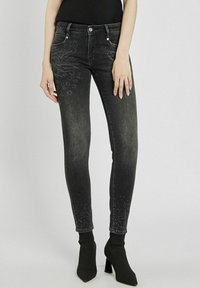 Wąskie czarne dżinsy z denimu z wzorem w panterkę z jednej strony oraz ozdobnymi detalami blisko dołu. Gładka tekstura z klasycznym krojem.